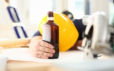 Arm of drunken worker in yellow helmet hold liquor