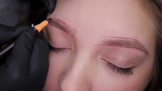 The permanent makeup artist sketches over the contour of the eyebrows to fix the permanent makeup. Permanent makeup procedure, performing PMU of eyebrows