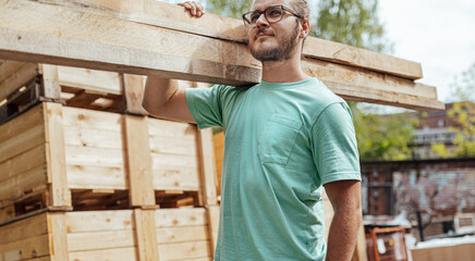 A man carrying wood, wearing a T-shirt with a wooded background.