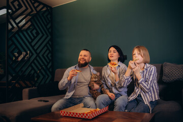 Excited Family cheering for their sport team on TV, Eating pizza in the living room at home. Fans with hands up and pizza slices in hands having fun watching favorite game on Television. Copy space