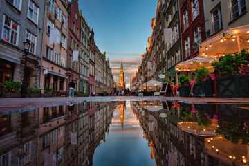 People are walking on the beautiful old town in Gdansk with historical city hall reflected in water, Poland.