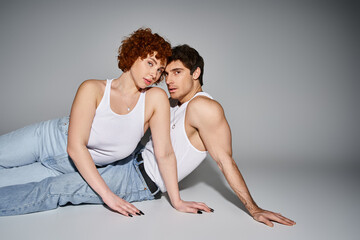 appealing sexy couple in comfy blue jeans reclining on floor together and looking at camera