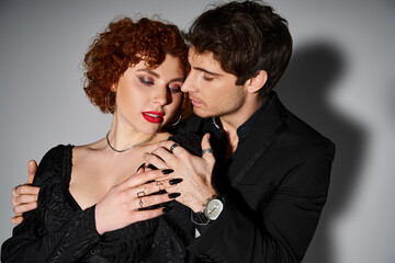 appealing girlfriend and boyfriend in debonair black attires hugging lovingly on gray background