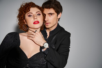 appealing sexy couple in elegant black attires posing passionately together on gray background