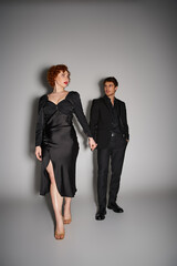 good looking loving couple in elegant black attires holding hands and posing on gray backdrop