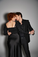 beautiful sexy couple in black elegant attires kissing and hugging lovingly on gray background