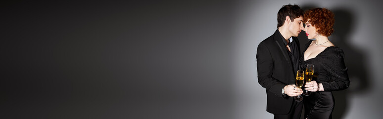 pretty woman in black dress hugging her handsome boyfriend on gray backdrop, champagne, banner