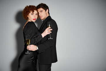 sexy good looking couple in black attire hugging and looking at camera with champagne in hands