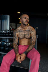 Fototapeta na wymiar Chico joven musculado y tatuado posando en gimnasio sin camiseta