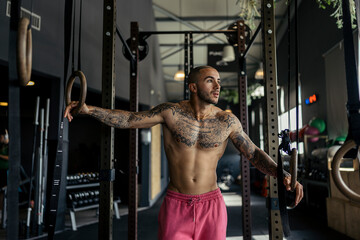 Chico joven musculado y tatuado posando en gimnasio sin camiseta