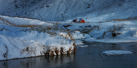 Red house in frozen, quiet valley by the shore in a soft winter light. Lofoten Islands, Northern Norway. 