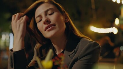 Beautiful woman sitting at cafe table on romantic date in evening. Attractive female on meeting in outdoor restaurant and city lights on background