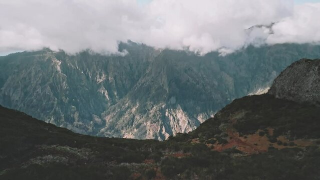 Drone flight over a cliff with the mountains in the background camera pan downwards revealing the town of Curral das Freiras, Madeira 01