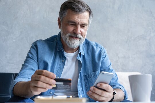 Smiling mature old man enjoying shopping in internet store using mobile phone applications