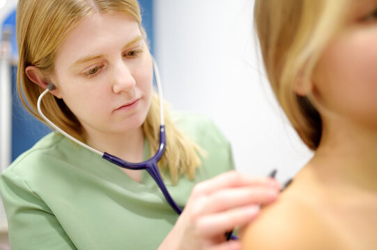 Caring female doctor with stethoscope listening to heartbeat and breathing of young girl. Schoolgirl patient is at pediatrician appointment. Treatment of viral and infectious diseases