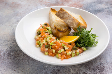 Salmon tartare with tomato and arugula on white plate