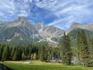 green meadows and a lake at the bottom of tall bare rock mountains
