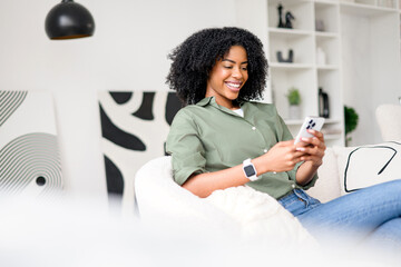 A relaxed African-American woman enjoys a moment of leisure, smiling as she scrolls through her...
