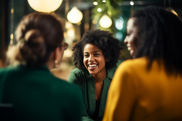 A group of women engaged in a lively conversation. The warm ambiance and blurred background  in a cafe or restaurant. The lighting highlights her face and the joyous interaction among the friends. - obrazy, fototapety, plakaty