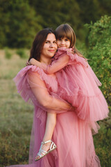 Naklejka premium Mother and her daughter in tulle pink dresses posing on nature at summer. Love