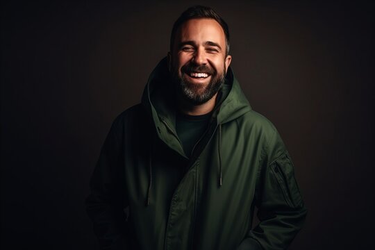 Portrait of a smiling bearded man in a green jacket on a dark background.