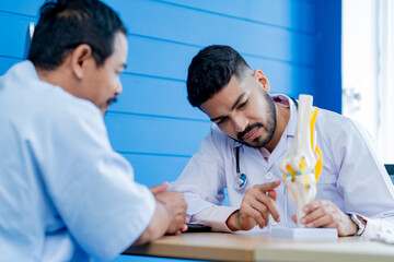 Asian male orthopedics professional doctor consulting explaining knee bone model to male patient, Physiotherapist explain an anatomical human knee-joint to an elderly patient. Concept physio treatment - obrazy, fototapety, plakaty