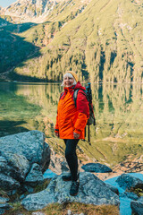 Lady tourist with a backpack standing on top of the mountain and enjoy the beautiful view of mountains Morskie Oko lake. Hiking travel and adventure in Poland, Tatry 