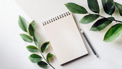 Blank white mockup sketchbook on white background, free space. Top view on empty rustic style notepad with green leaves,pencil on table, copy space for text or advertisement.