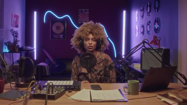 UCC of African American woman hosting online show or vlog and looking at camera at home recording studio with neon lights at night