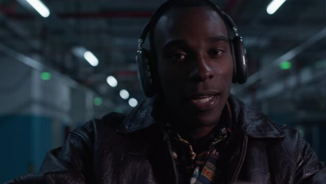 Black Afro-American male singer hip pop rapper moves to the beat. Looking staring in to camera, wearing modern headphone in modern underground metropolitan garage parking.