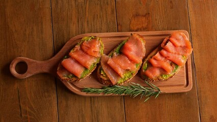 On wooden board are selectable toasts with red fish and creamy avocado Indulge in taste of fish complemented by the avocado Enjoy rich flavors of fish and avocado combination for a delicious lunch