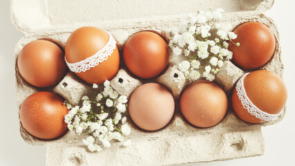 Brown Easter eggs decorated lace and white gypsophila flowers in carton on white background. Easter...