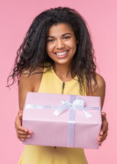 Vertical portrait of happy smiling beautiful birthday girl posing with decorated present box in hands over pastel pink background