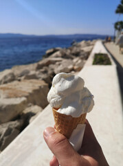 A hand holding an ice cone in the foreground. Beautiful deep blue ocean in the background