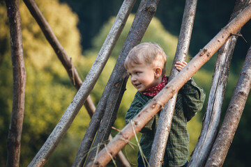 Little Cute Blond Boy Hiding between Wooden Logs - 745786818