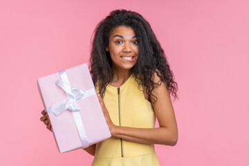 Studio portrait of cute coquette girl posing over pastel pink background with decorated gift box in hands - 745787094