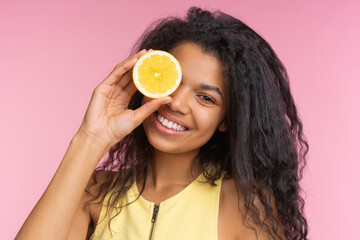 Close up studio portrait of beautiful happy smiling girl posing over pastel pink background with a lemon cut in a half in hand - 745787205