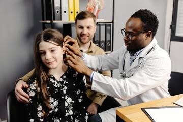 Doctor inserting a hearing aid into a young girl's ear in doctor's office