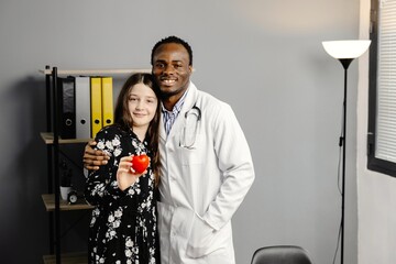 Man in white robe and girl standing together, girl holding red heart