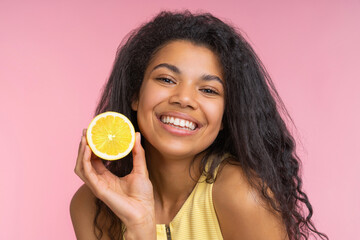 Close up studio portrait of beautiful happy young woman with charming smile posing over pastel pink background with a lemon cut in a half in hand - 745787221
