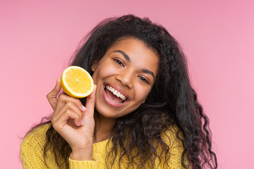 Close up studio portrait of cute happy smiling girl posing over pastel pink background with a lemon cut in a half in hand - 745787258
