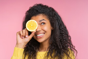 Close up studio portrait of attractive coquette young woman with charming smile posing over pastel pink background with a lemon cut in a half in hand - 745787263