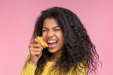 Portrait of beautiful young african american woman posing over pastel pink background pretending to bite a lemon cut in a half - 745787289