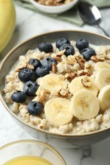 Tasty oatmeal with banana, blueberries, walnuts and milk served in bowl on white marble table, closeup