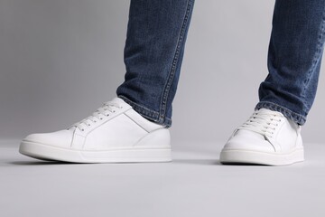Man wearing stylish white sneakers on grey background, closeup