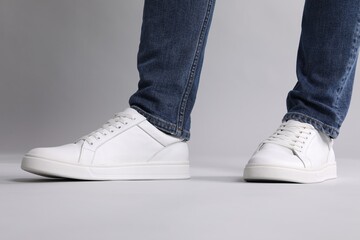 Man wearing stylish white sneakers on grey background, closeup