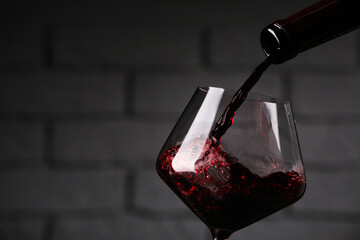 Pouring tasty red wine from bottle into glass against brick wall, closeup. Space for text