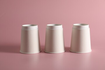 Shell game. Three paper cups on pink background