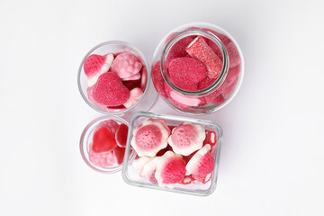 Different yummy pink candies in glass jar and bowls on white background, flat lay