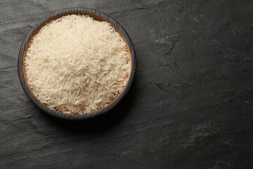 Raw basmati rice in bowl on black table, top view. Space for text